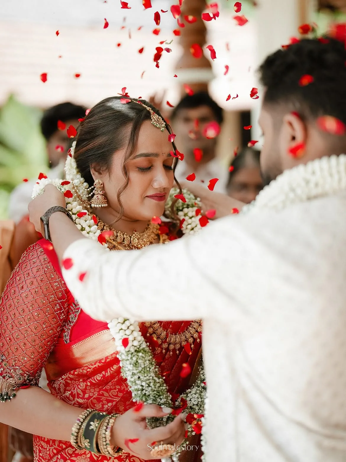 A couple exchanging flower garlands beneath falling rose petals
